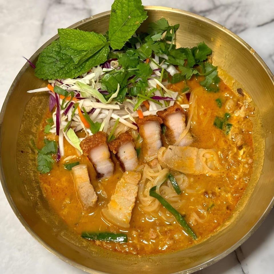 So Saap's Thai noodle dish with crispy pork belly, red curry, and fresh herbs in a brass bowl.