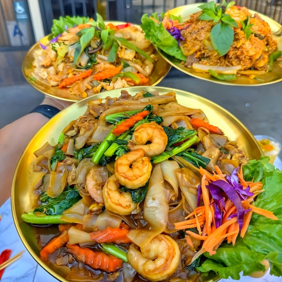 Three golden plates of Thai noodles and rice dishes, garnished with fresh herbs and vegetables.