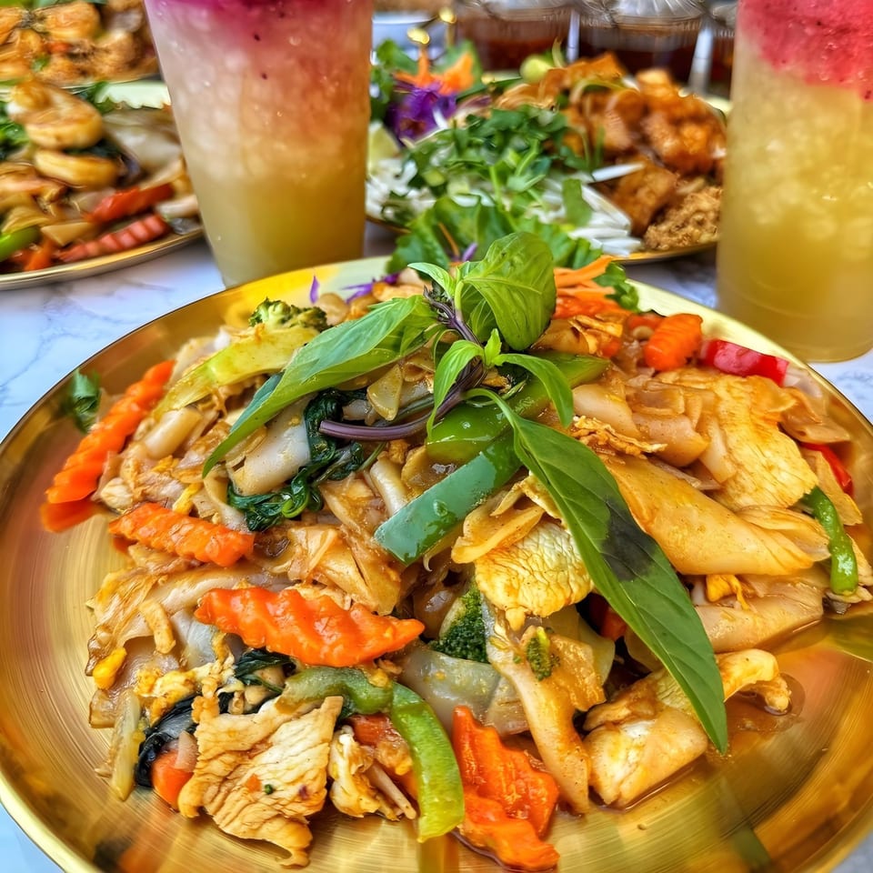 A golden plate of So Saap Pad See Ew with chicken, wide noodles, and vegetables, garnished with basil.