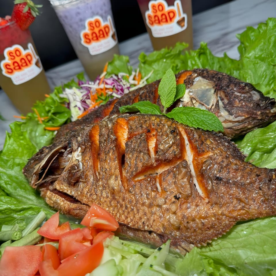 Two whole fried fish on lettuce with mint, tomatoes, and So Saap branded drinks.